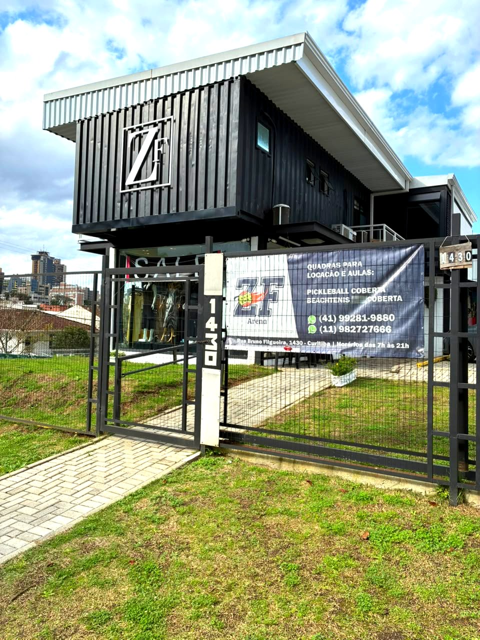 Fachada de entrada do Espaço Zu Feres, prédio em container preto, com placa da ZF Arena no portão